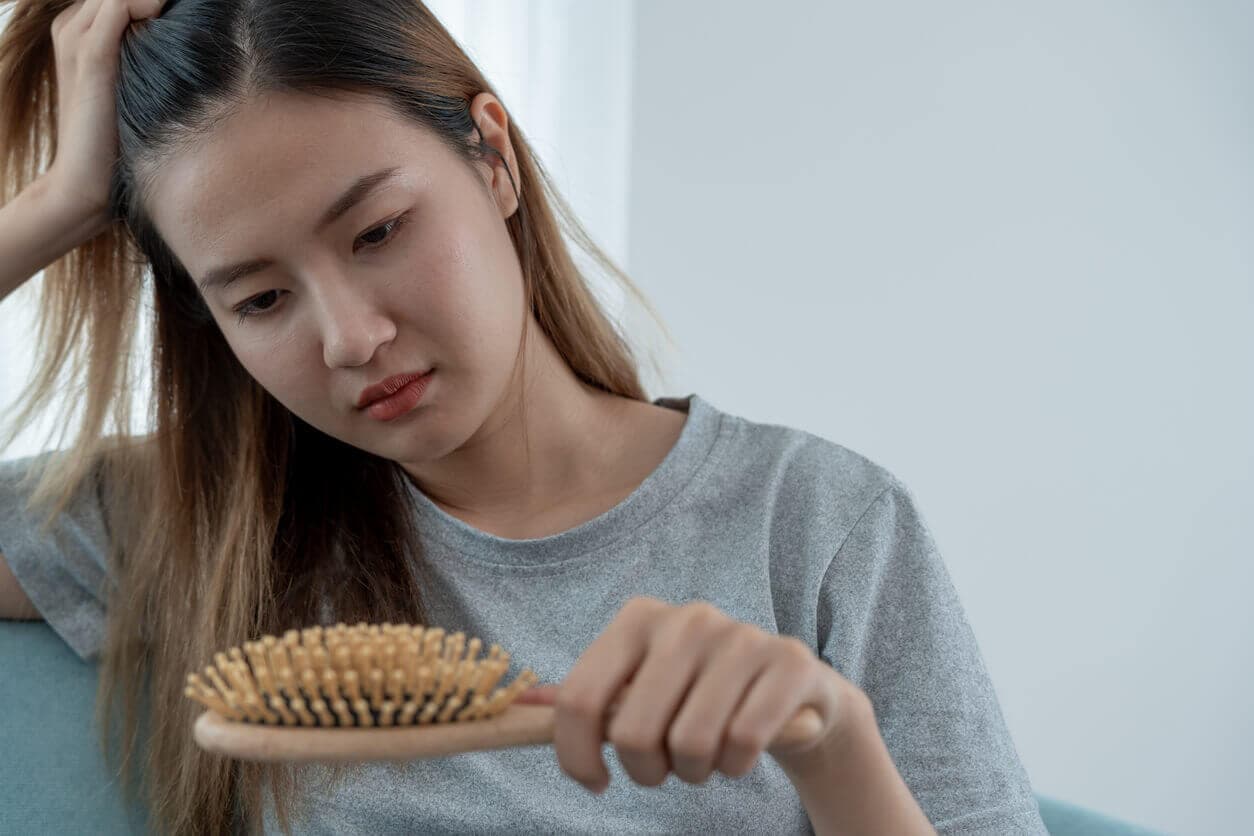 Mulher, com uma escova de cabelo na mão, demonstrando ansiedade e estresse ao verificar um quadro de queda de cabelo