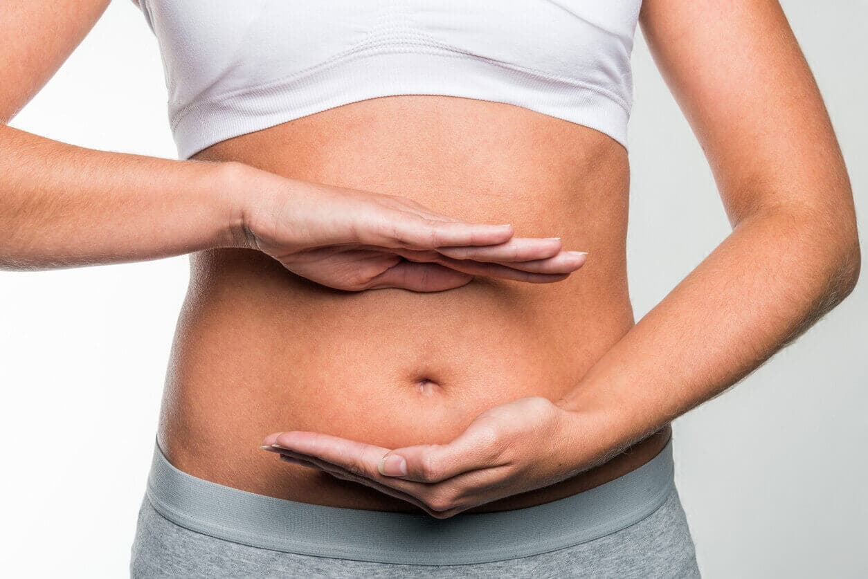Close do abdomen de uma mulher, com as mãos na frente da barriga, evidenciando o inchaço no local