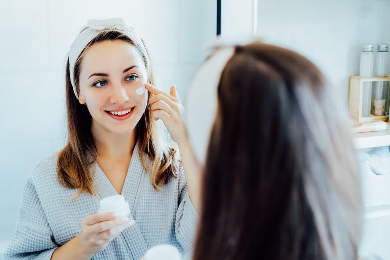 Mulher jovem em frente ao espelho, com um roupão após o banho, fazendo skincare