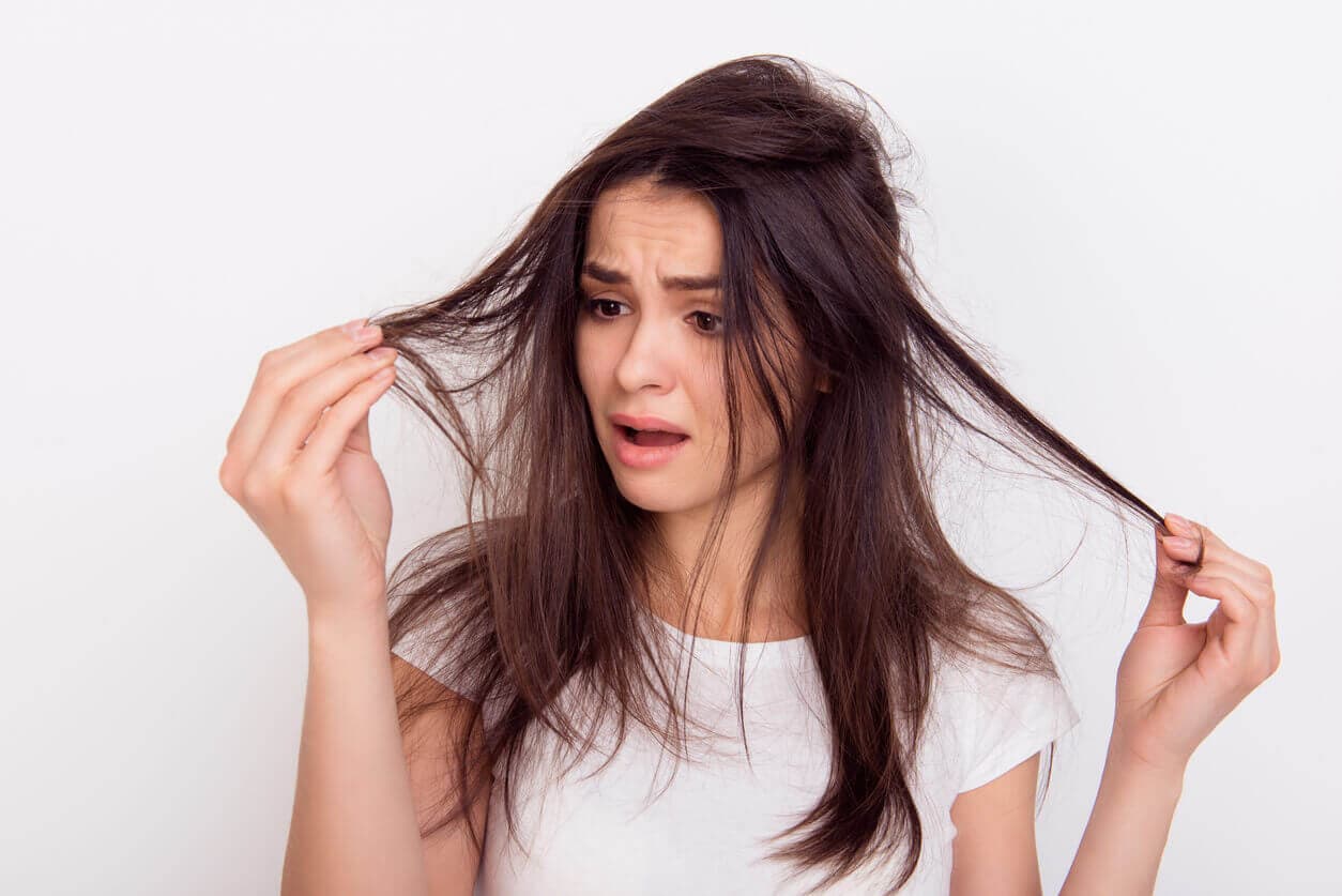 Mulher tocando as mãos em mechas finas do cabelo, demonstrando preocupação com a baixa densidade capilar