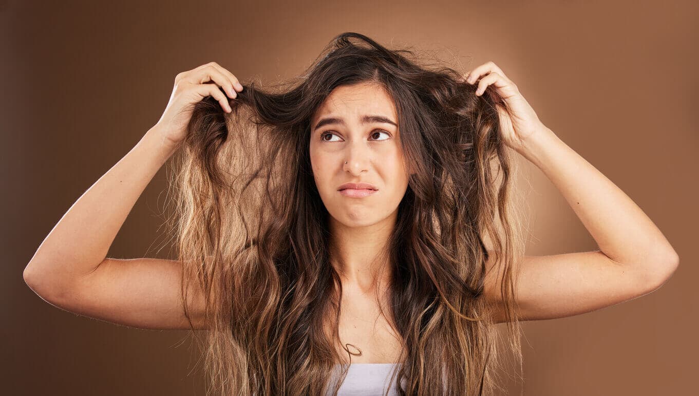 Mulher jovem segurando mechas do próprio cabelo com uma expressão triste e de insatisfação