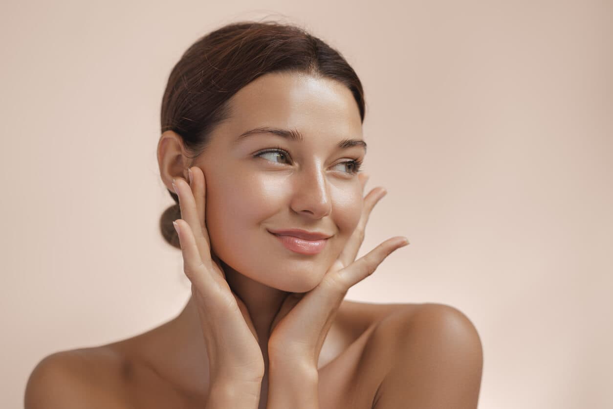 Paciente do sexo feminino com as mãos no rosto evidenciando o rejuvenescimento facial após o procedimento de lifting