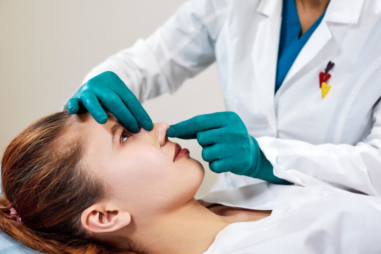 Jovem deitada durante atendimento enquanto médica cirurgiã faz preparações para realizar a rinoplastia