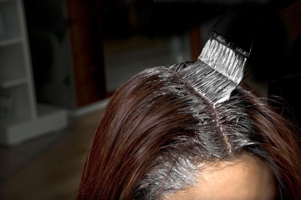 Topo da cabeça de uma mulher com um pincel aplicando tintura no cabelo