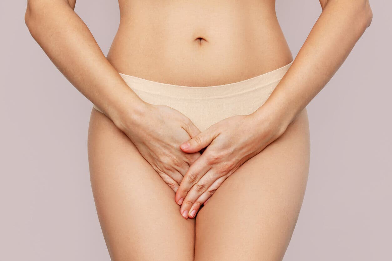 Mulher de calcinha bege cobrindo a região íntima com as mãos, simbolizando cuidado e privacidade