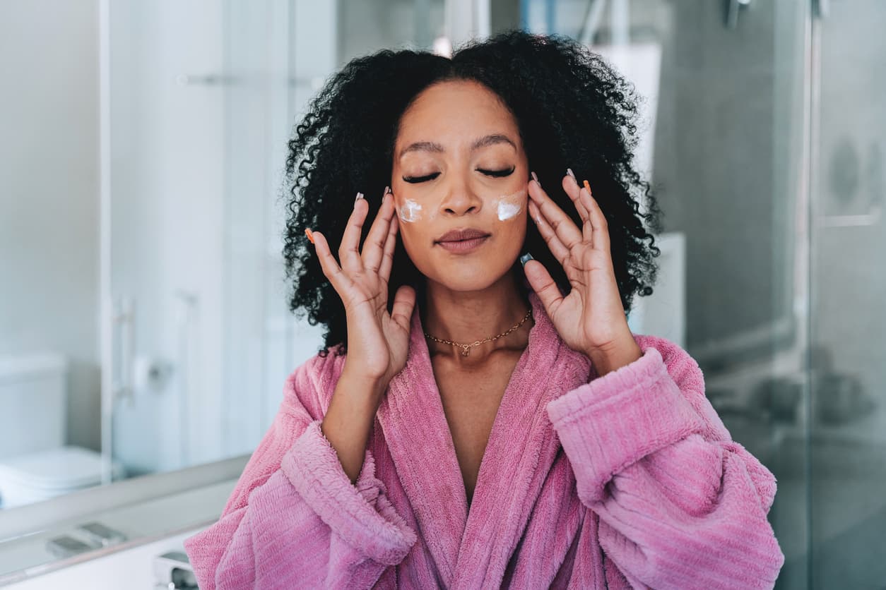 Mulher vestida com um roupão rosa em um momento de cuidado com a pele, realizando rotina de skincare