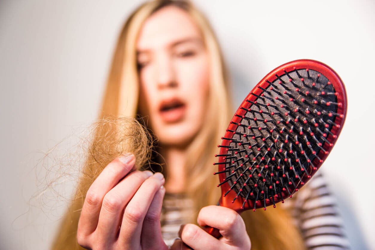 Mulher preocupada segurando uma escova de cabelo cheia de fios soltos, representando sinais de queda capilar intensa, possível início de calvície